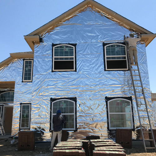 Two-story home wrapped in reflective barrier